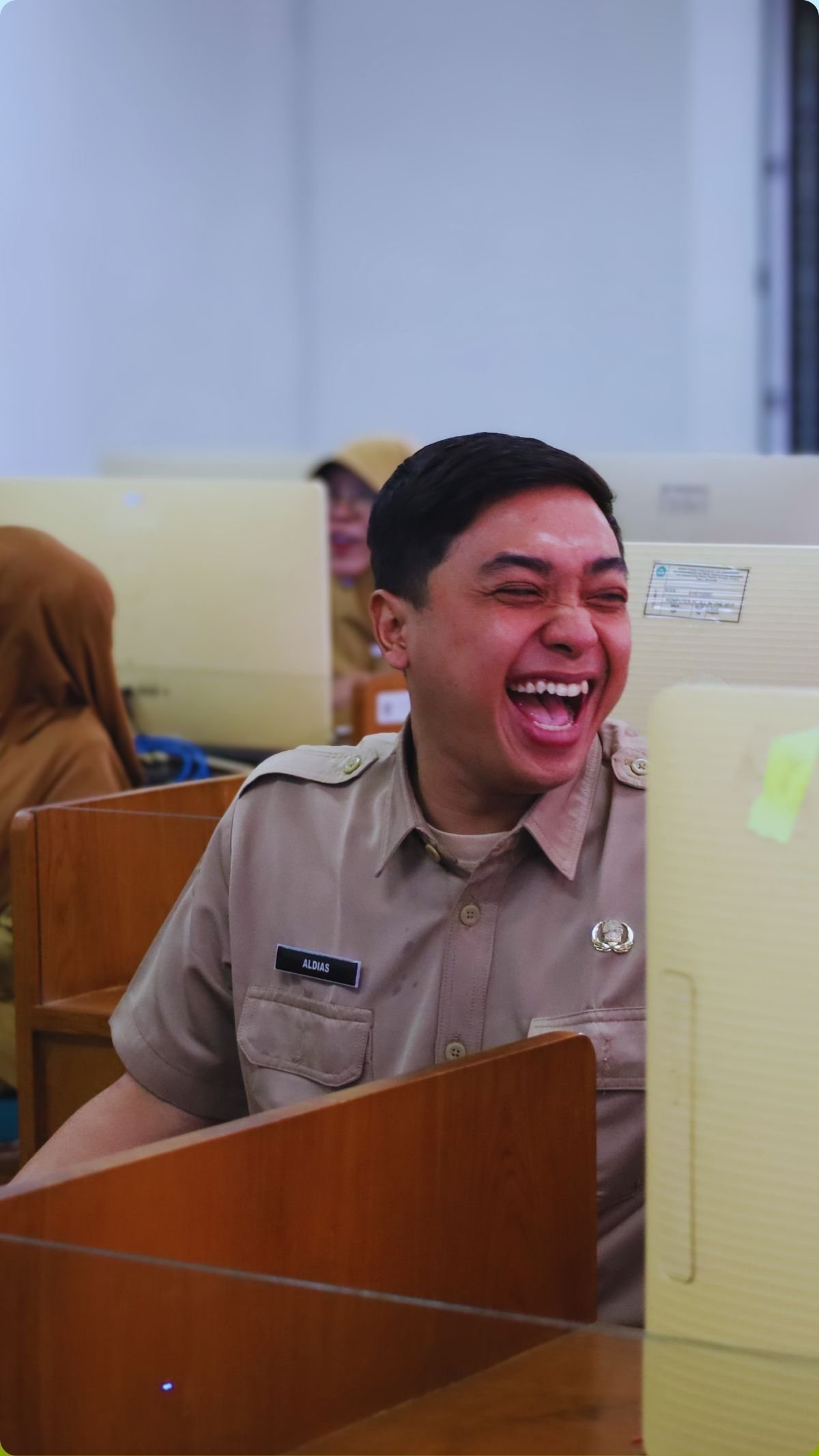 Peserta laki-laki tertawa dalam sesi kegiatan laboratorium komputer.