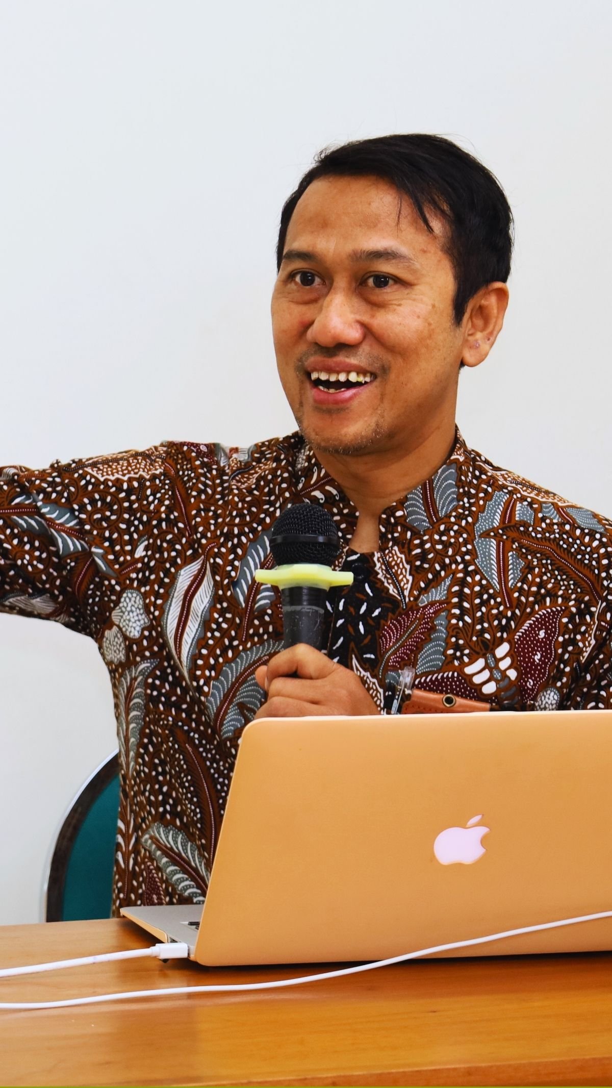 Fasilitator laki-laki menyampaikan materi dengan mikrofon dan laptop.